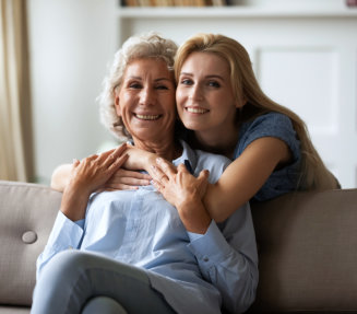 a female hugging an elderly woman sitting on a sofa