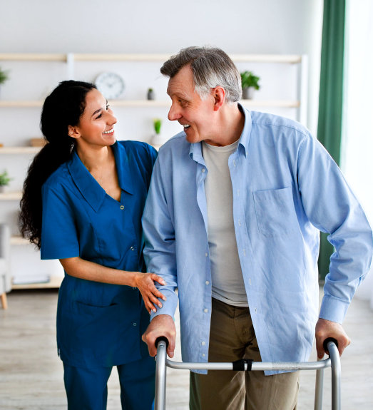 A female caregiver assisting an elderly man to walk