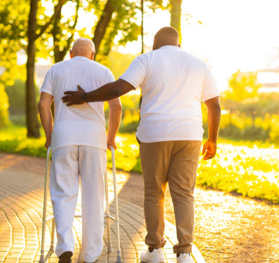 a male assisting an elderly man to walk outside