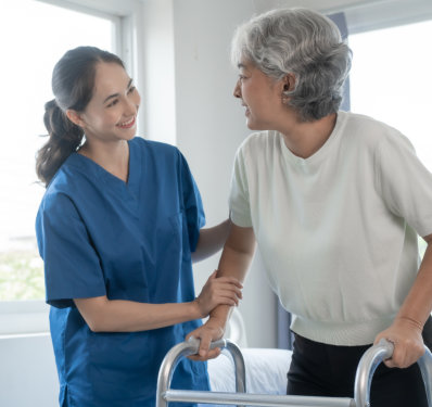 A female caregiver assisting an elderly woman to walk