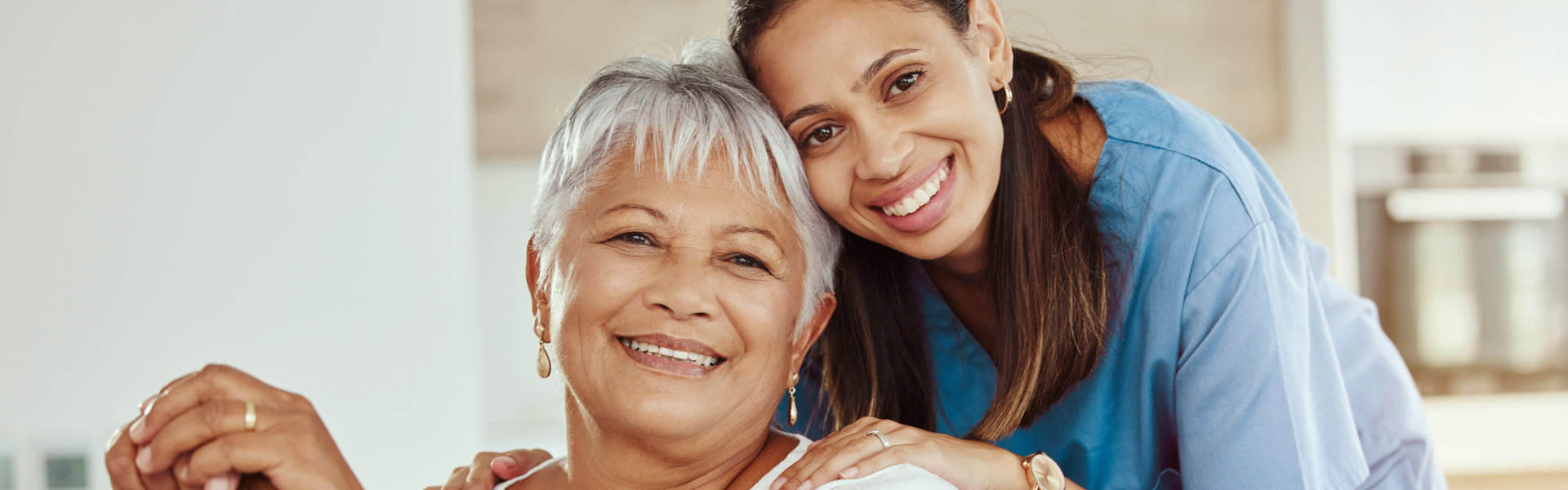 an elderly woman sitting and a female caregiver smiling together