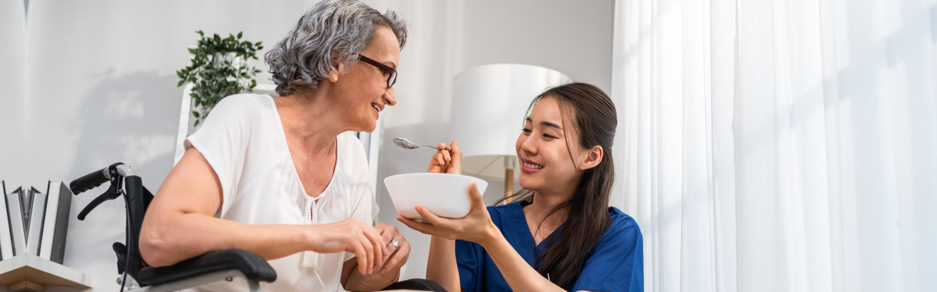 A female caregiver feeding an elderly woman