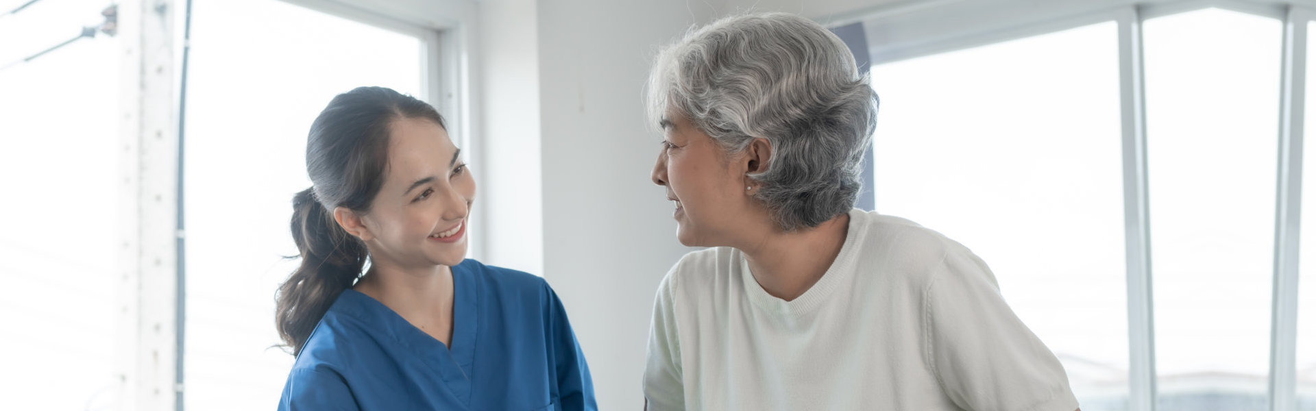 A female caregiver assisting an elderly woman to walk